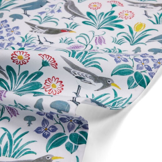 Detail of tea towel with a pattern of birds and flowers in muted colours on white background.  